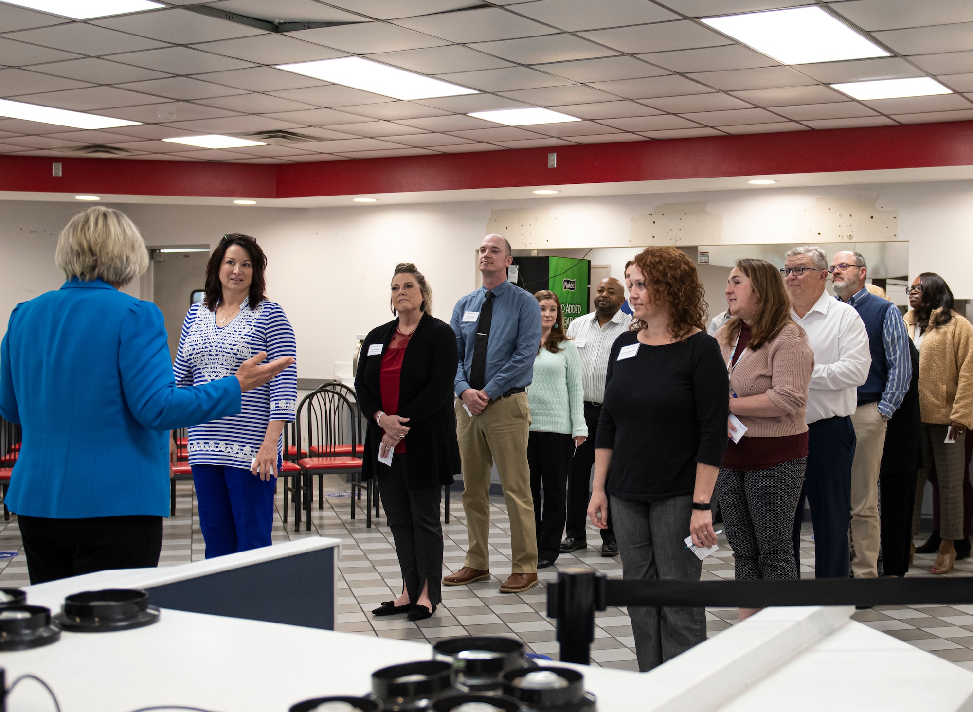 Group of people standing, facing forward toward one woman on the left side.