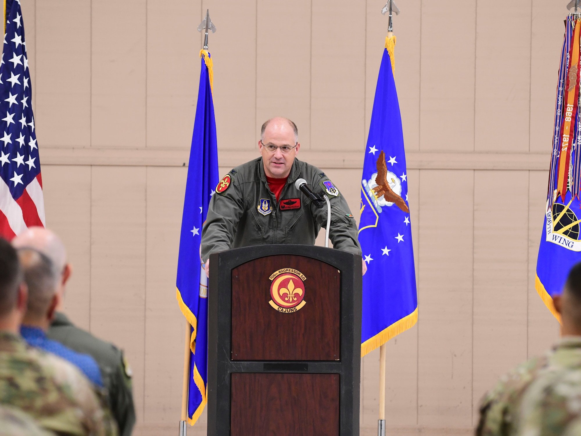 Col. Sean Rassas speaks behind a podium during a ceremony. The U.S. Air Force, 10th Air Force, and U.S. flags are behind him.