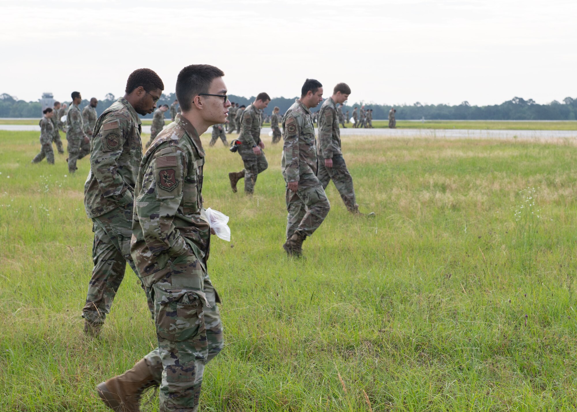 Airmen walk through grass looking for debris.