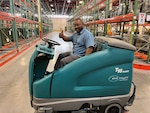 Man giving a thumbs up while sitting on an autonomous floor scrubber in a warehouse.