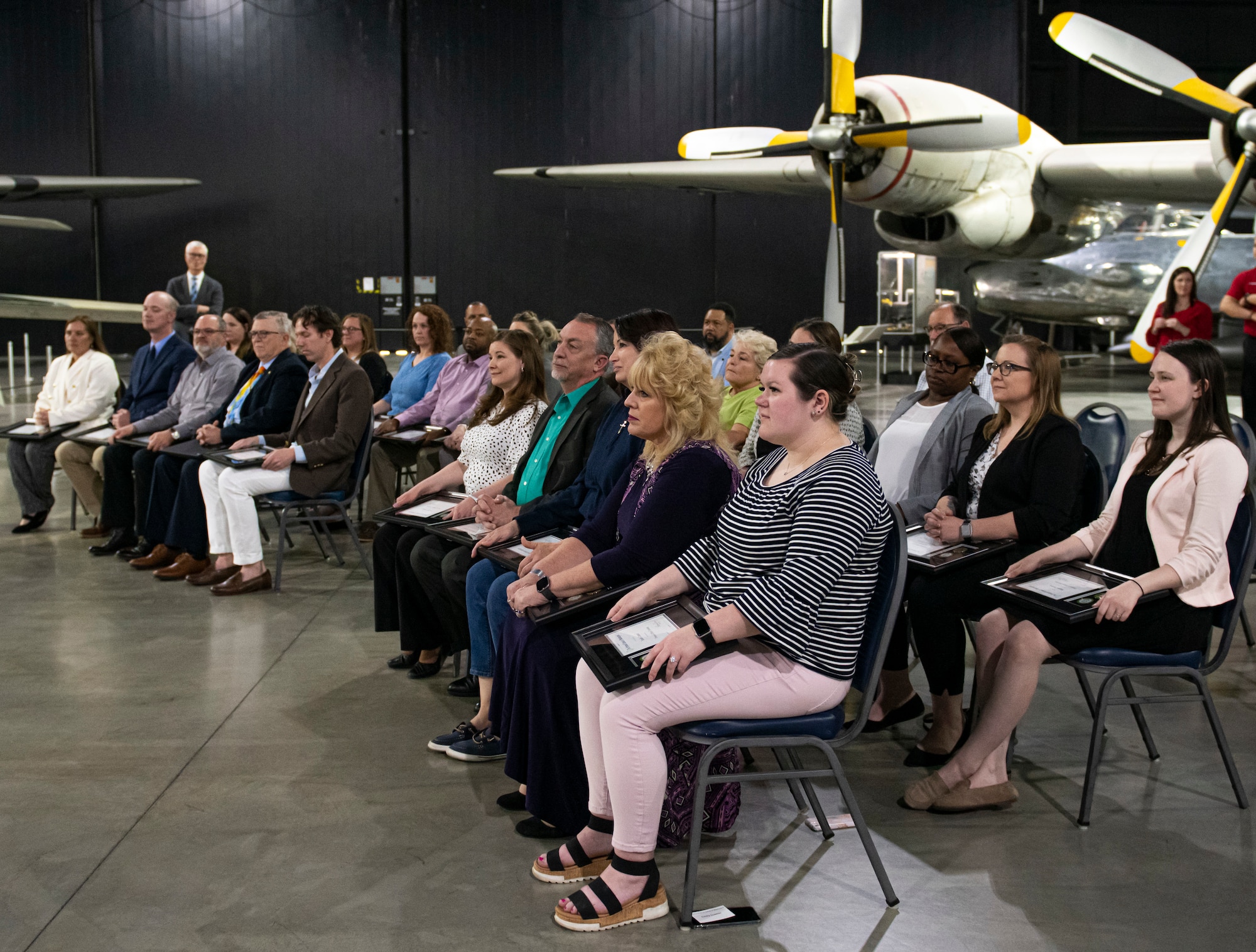 Group of people sitting in chairs in front of aircraft in the top right corner.