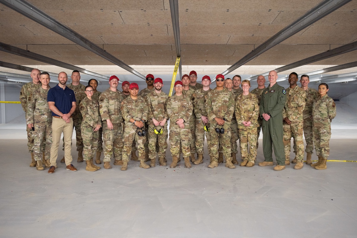 A group of men and women in uniform pose for a group photo on a firing range