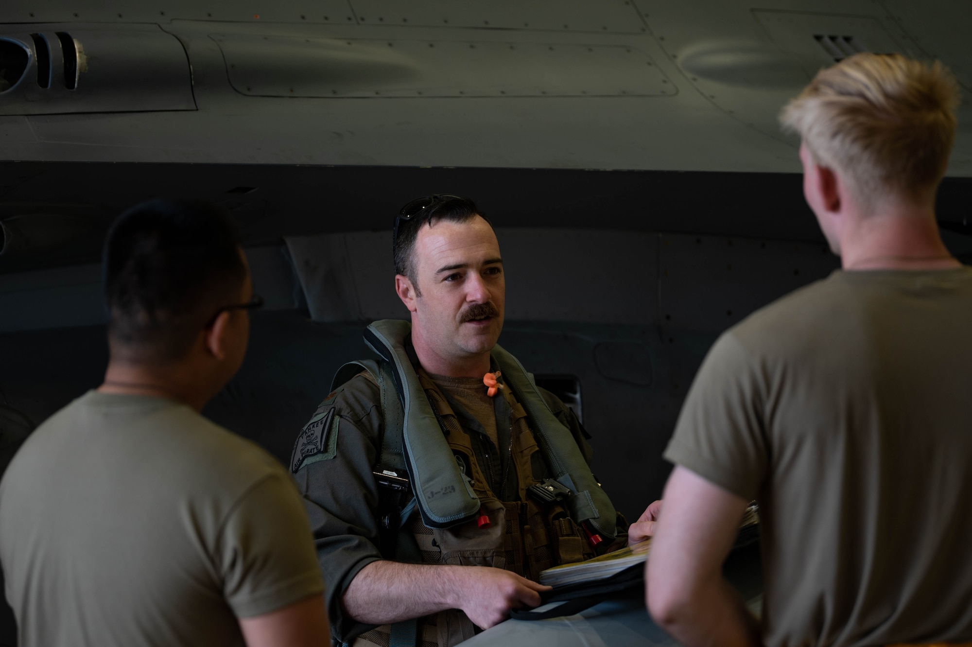 mustached man talks to two other men