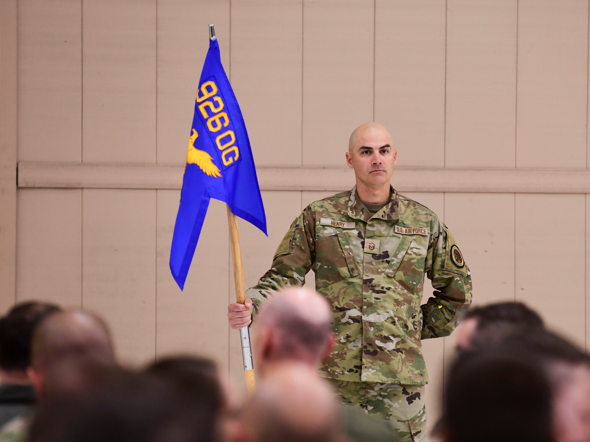 Master Sgt. Jacob Henry stand in front of the crowd while holding the guidon. The guidon has a blue flag that reads "926 OG" in gold letters.