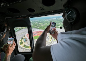 Two men take pictures with their phones while flying in a helicopter.