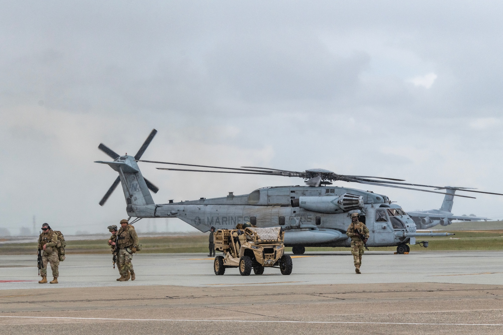 Airmen in front of a vehicle and a helicopter