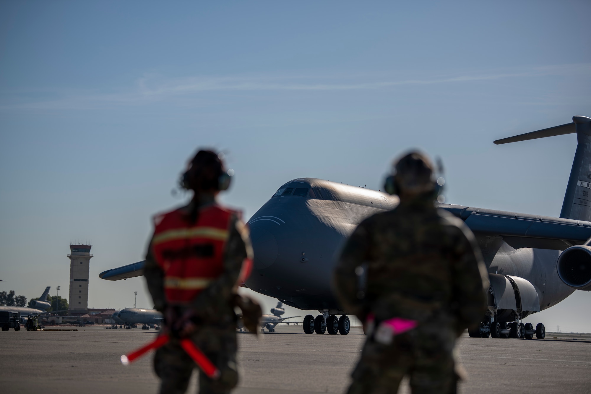 Blurred figures stand on a flight line with a very large military aircraft in front of them
