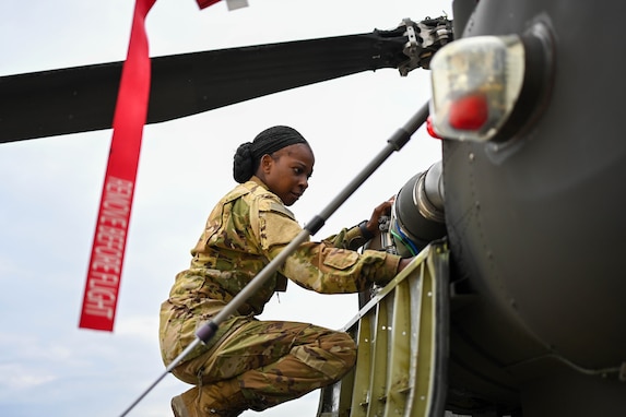 A soldier squats down while inspecting an Apache helicopter.