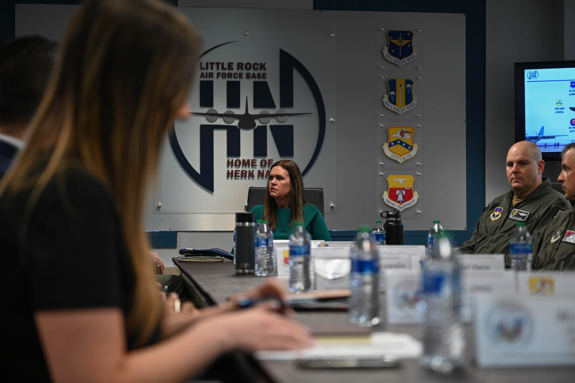 A woman sits at a table with people in uniform.