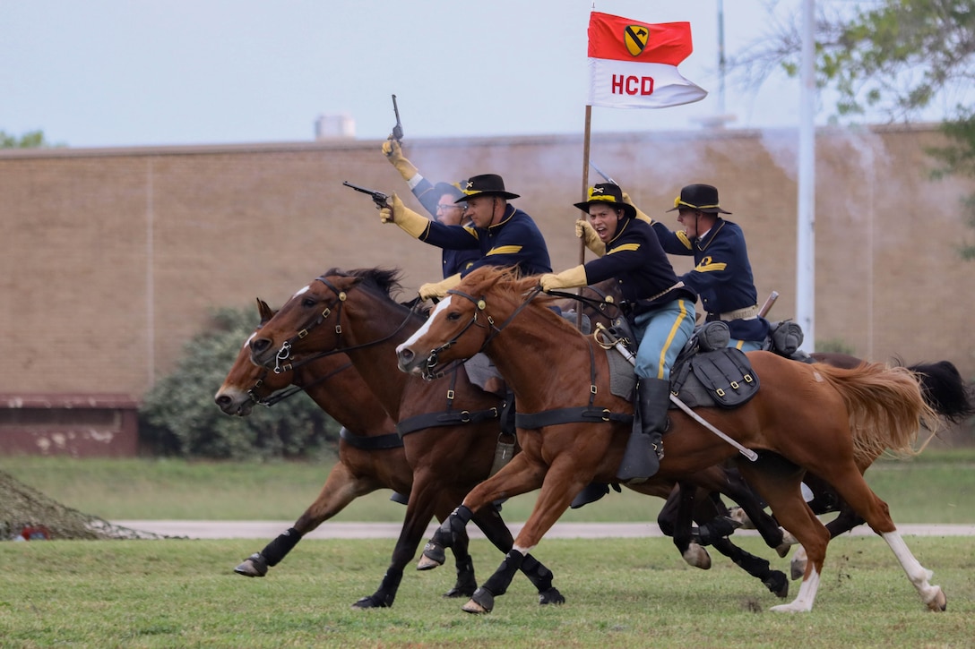 Soldiers on horses run across a field while firing guns.