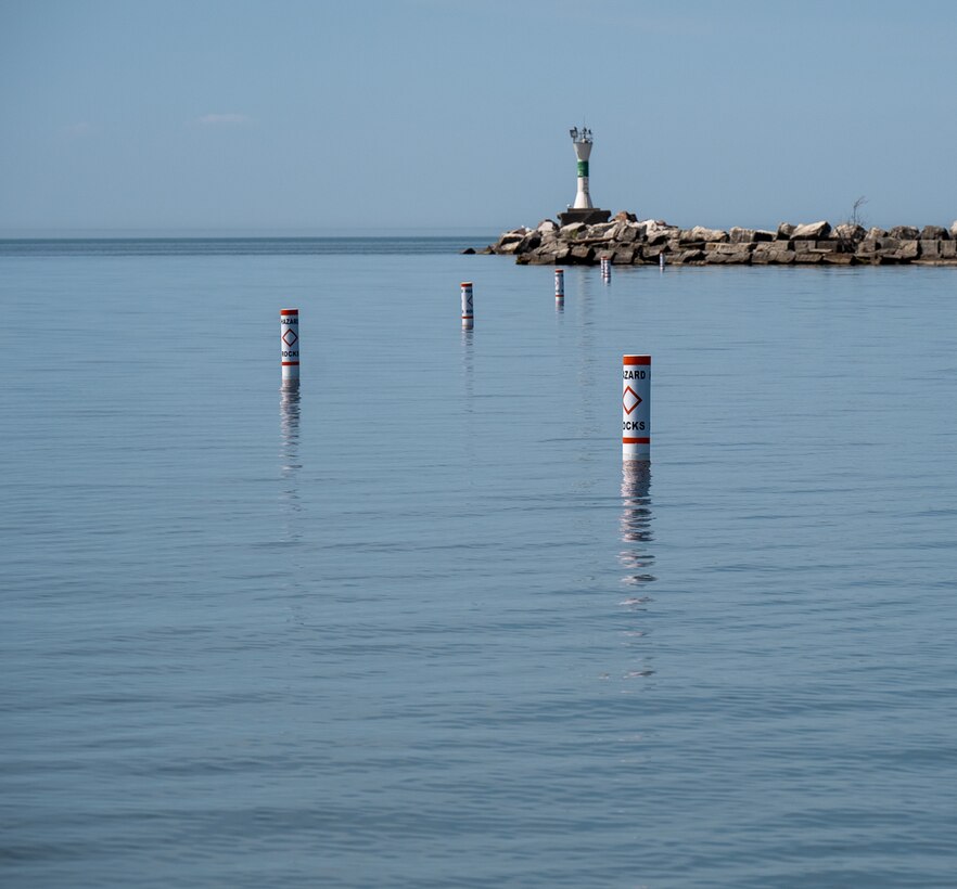 Buoys floating along the waters of Ashtabula Harbor towards the lighthouse marking the location of a submerged stone wall below.