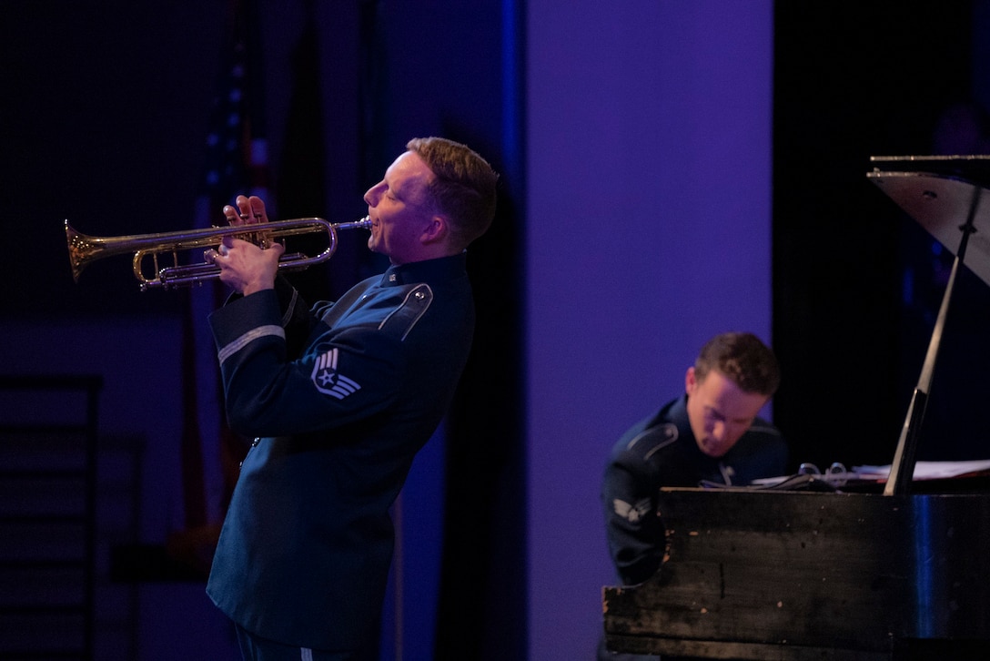 An airman plays an instrument as another airman plays the piano in the background.