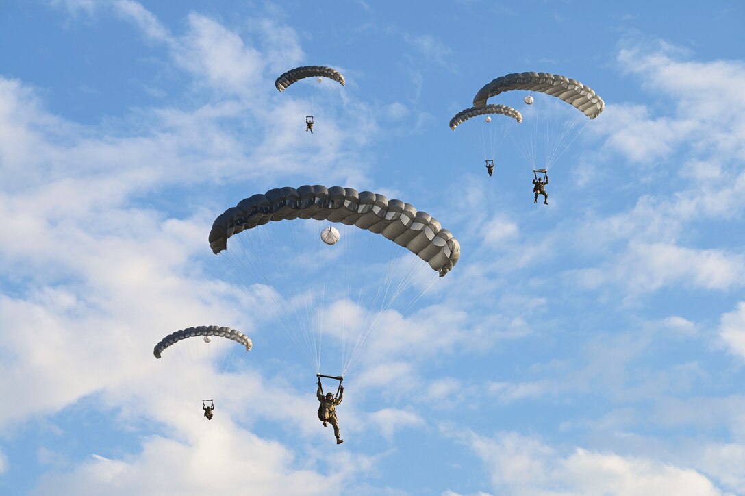 Five airmen free-fall in tandem with parachutes as seen from below.