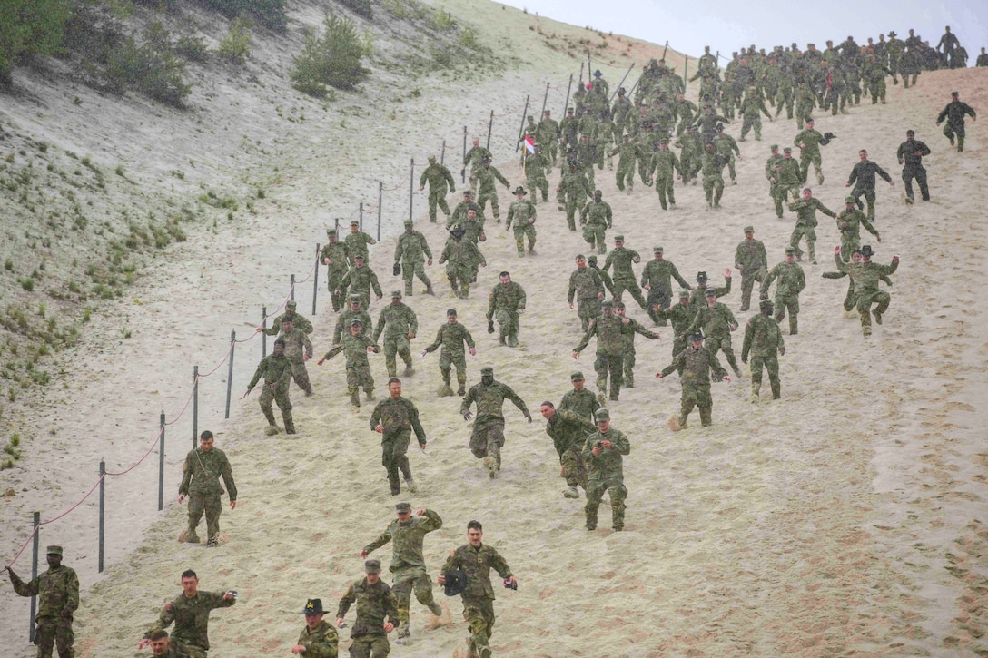 Soldiers run down a sandy hill.