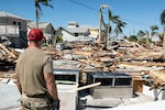 Man stands facing mounds of debris under a blue sky