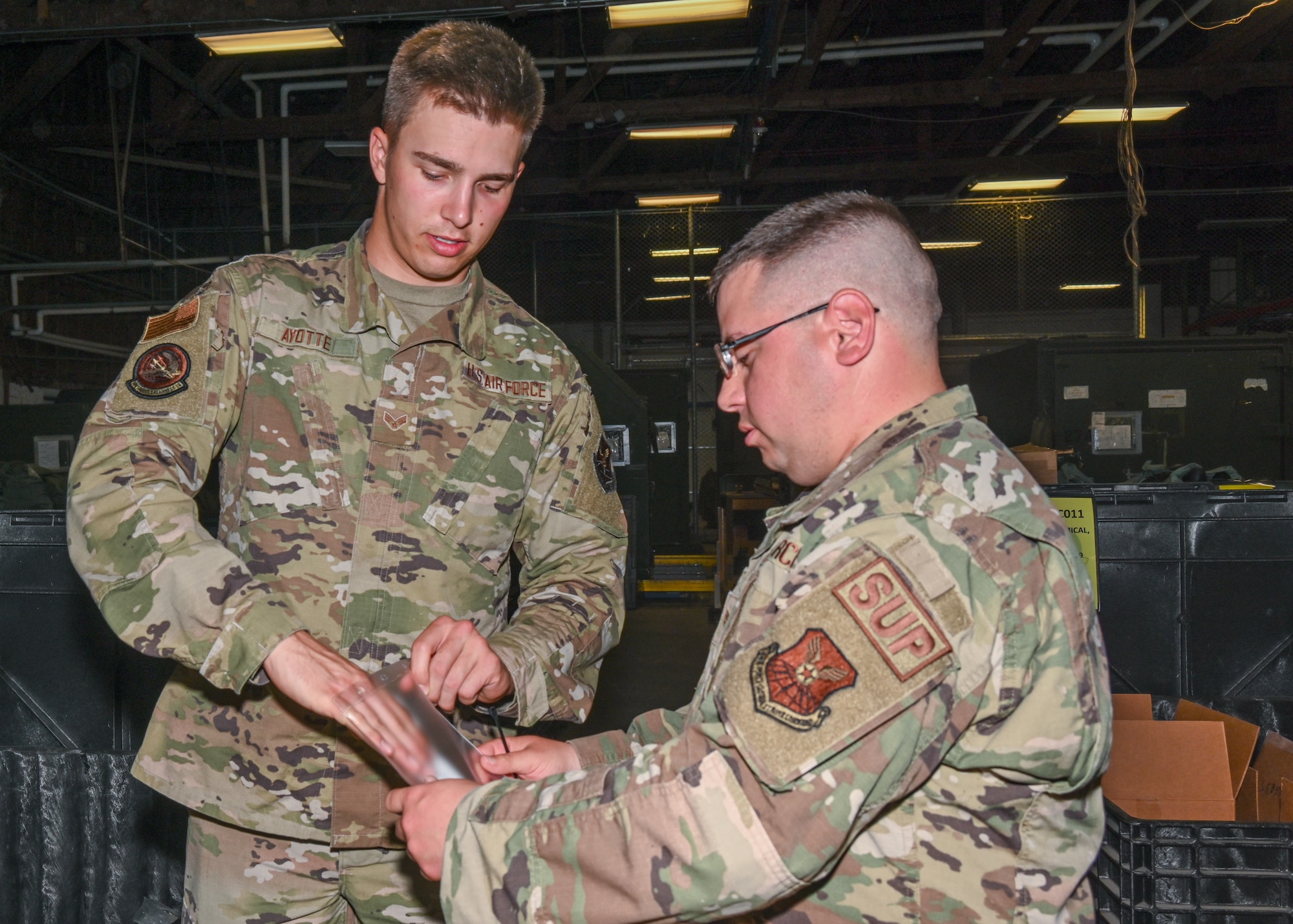 U.S. Air Force Senior Airman Dylan Ayotta, 509th Logistics Readiness Squadron, Individual Protective Equipment technician and U.S. Air Force Staff Sgt. Eric Cassity, 509th LRS, IPE supervisor attach the name of the member who a completed deployment kit is issued to at Whiteman Air Force Base, Missouri, May 9, 2023. Having the deployment kit already issued to the member will save about 200 man-hours for deployed personnel. (U.S. Air Force photo by Airman 1st Class Hailey Farrell)