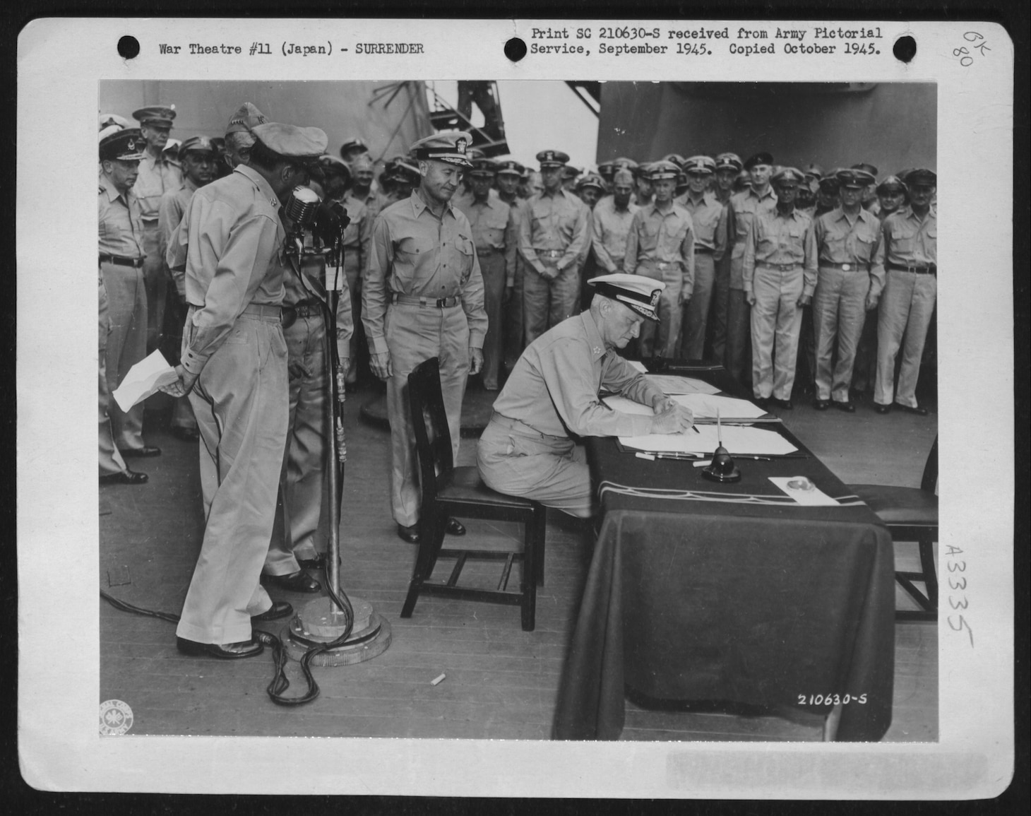 Fleet Admiral Chester W. Nimitz signs for the United States during the surrender ceremonies aboard USS Missouri in Tokyo Bay, ca. September 1945. At the microphone (left) is Army Gen. Douglas MacArthur. Image courtesy National Archives and Records Administration (342-FH-3A03335-117348AC)