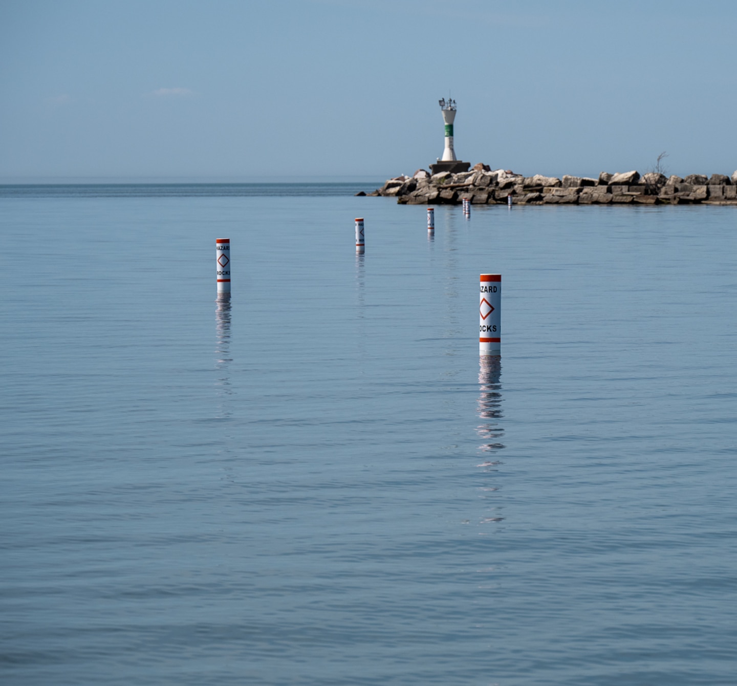 Buoys floating along the waters of Ashtabula Harbor towards the lighthouse marking the location of a submerged stone wall below.