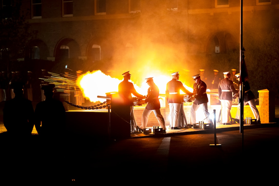 Marines fire cannons at night sending flames shooting into the air.