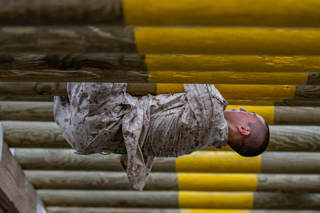 A Marine Corps recruit holds onto the underside of a log during an obstacle course.