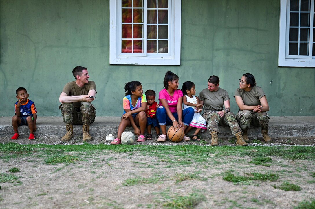 Three service members sit and talk with children.