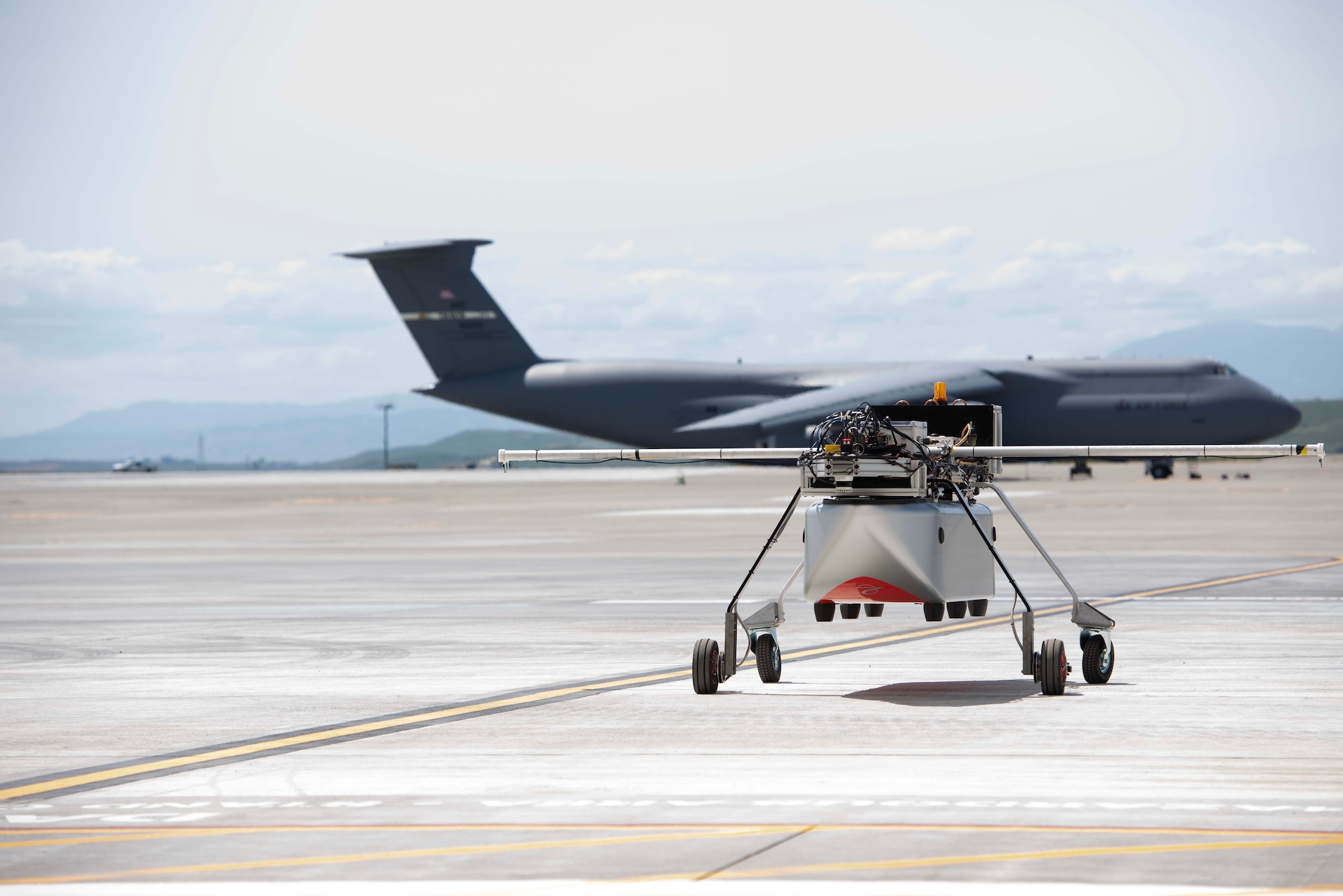 A robotic vehicle on the flightline with a military aircraft in the backgroud