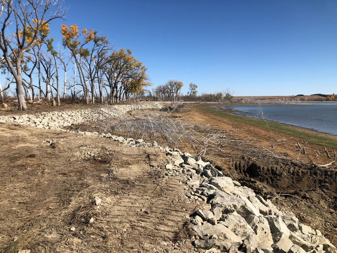 Rock can be seen along the shoreline of Harlan County Lake with trees in the left background and the lake in the right background.