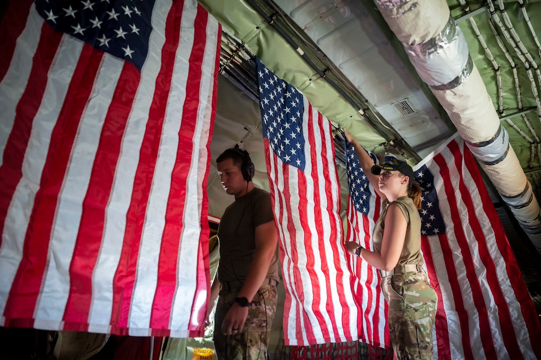 An airman hangs an American flag next to fellow flags hanging in formation aboard an aircraft.