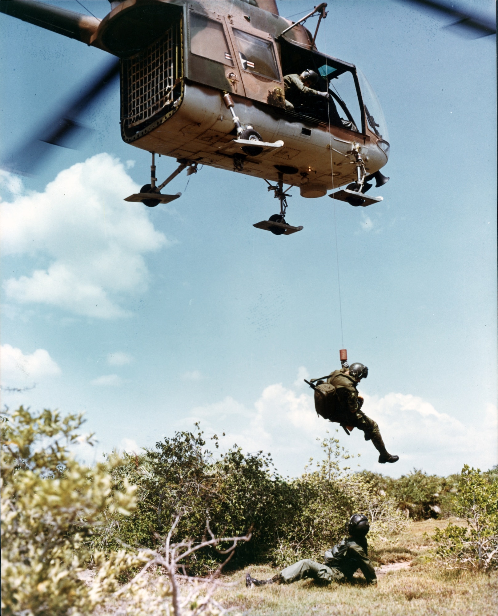 An Air Force pararescue specialist is lowered on a forest penetrator from an HH-43 to treat an injured pilot in Southeast Asia.