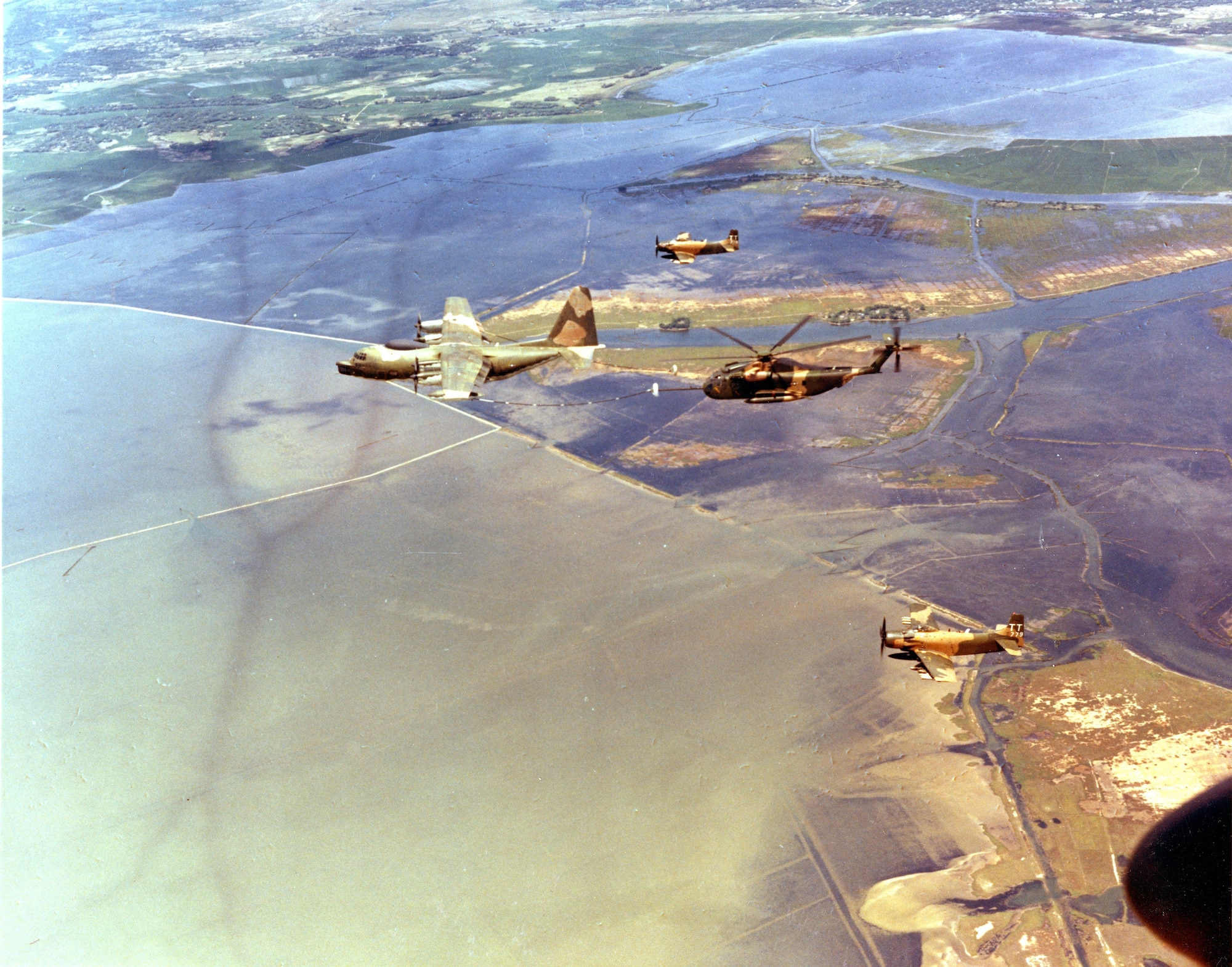 In flight over Southeast Asia, a US Air Force HC-130P refuels helicopters of the 37th ARR squadron, as two A-1's fly escort.