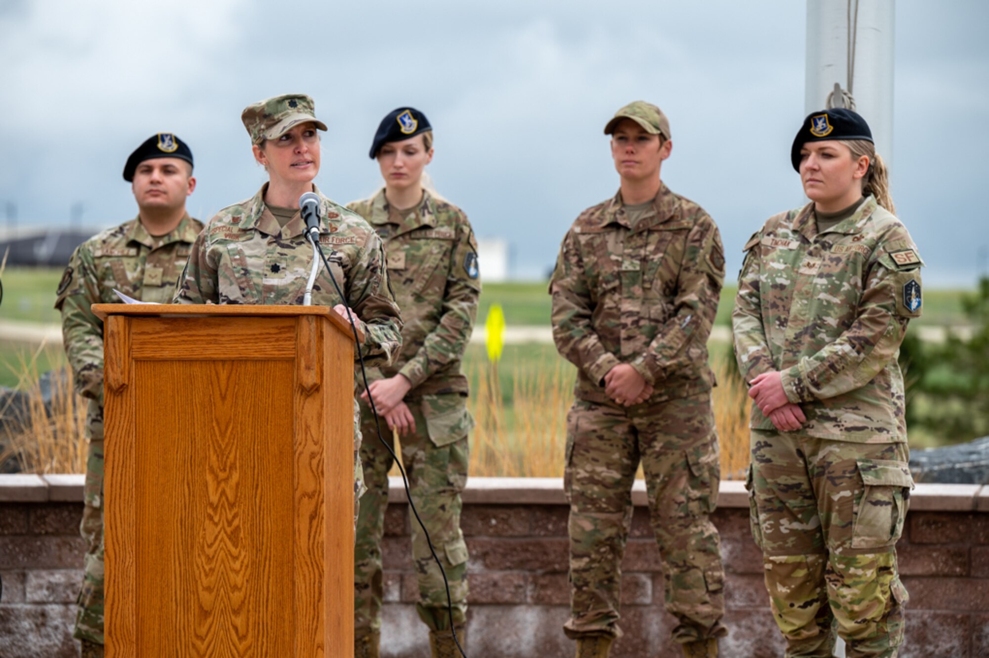 Members stand in front of a podium as one individual speaks.