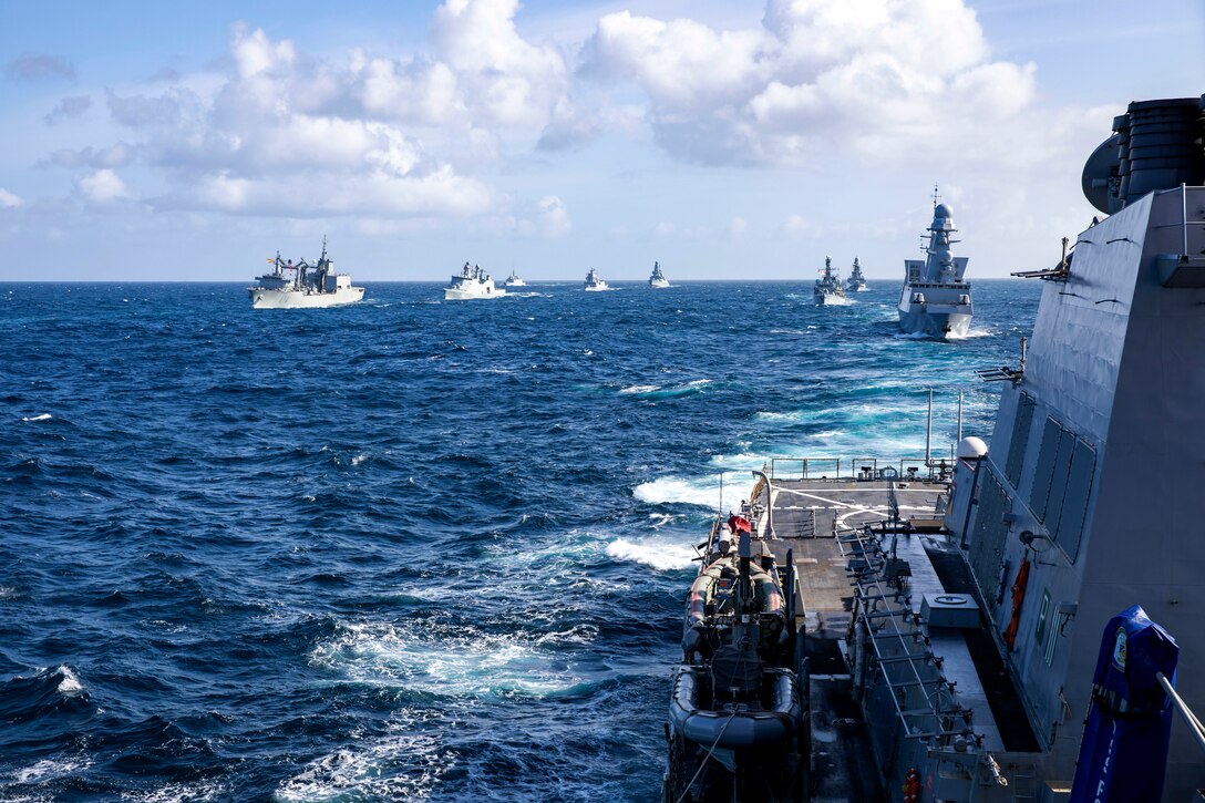 A group of ships sail in formation across the ocean.