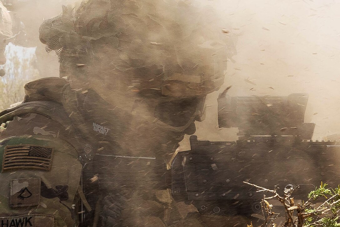 A soldier is seen through dirt and dust while firing a weapon during a training exercise.