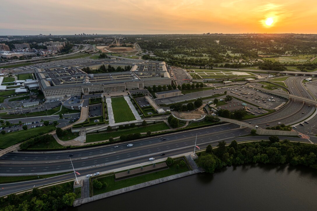 An aerial view of the Pentagon and surrounding areas, with orange sky as the backdrop.