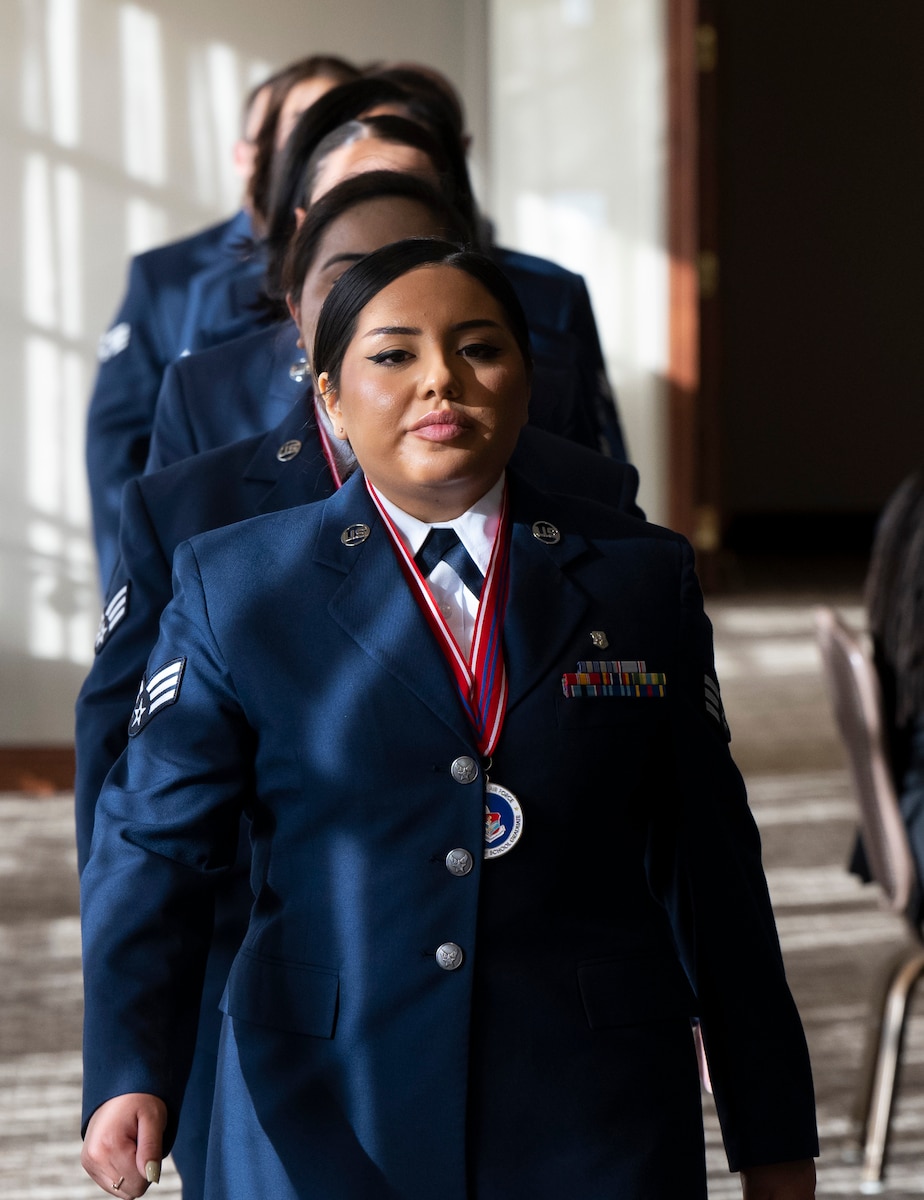 A woman in an Air Force uniform and with a medallion around her neck, leads airman in a single file.