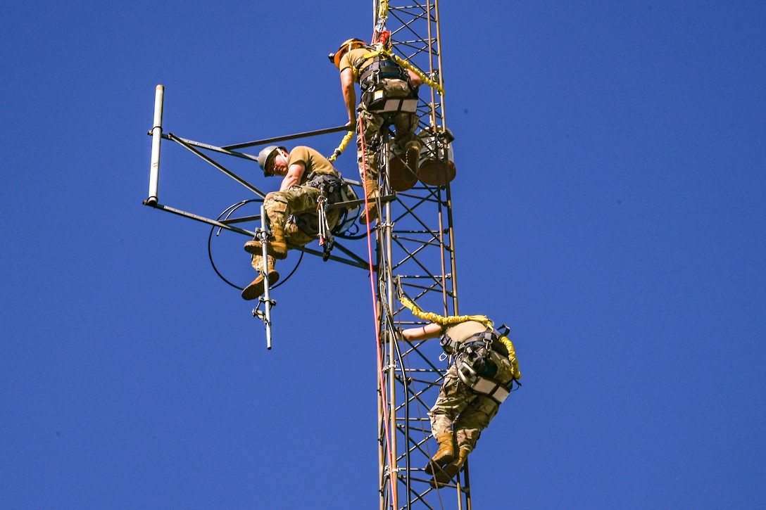 Three airmen climb a tower to install an antenna.