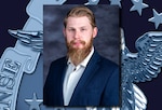 Headshot of a man with red hair and light skin wearing a white dress shirt and blue suit coat.