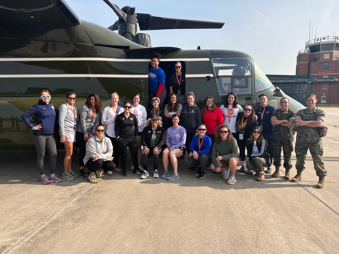 Female coaches from organizations like WeCOACH, American Volleyball Coaches Association and National Junior College Athletic Association stand in front of a MV-22B Osprey from Marine Helicopter Squadron One at Marine Corps Air Facility Quantico, Va,. before taking an orientation flight as part the command's Coaches Workshop. The event is designed to give attendees a firsthand look at what it takes to become a Marine Corps officer and an inside look at how Marines train. This included various activities and training exercises to help coaches better understand how they can apply learnings to their teams.