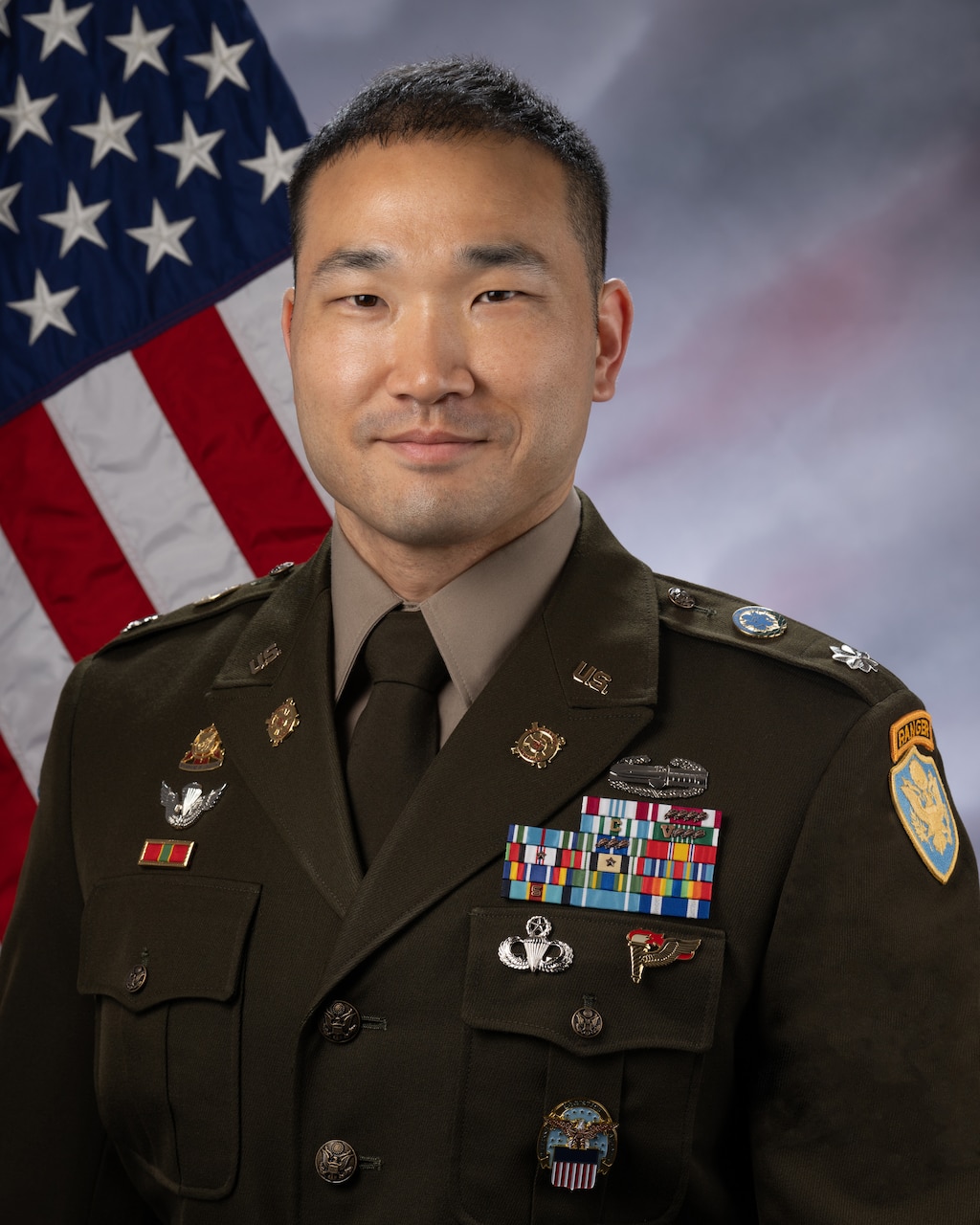 A uniformed service member poses for a photo with a flag in the background.