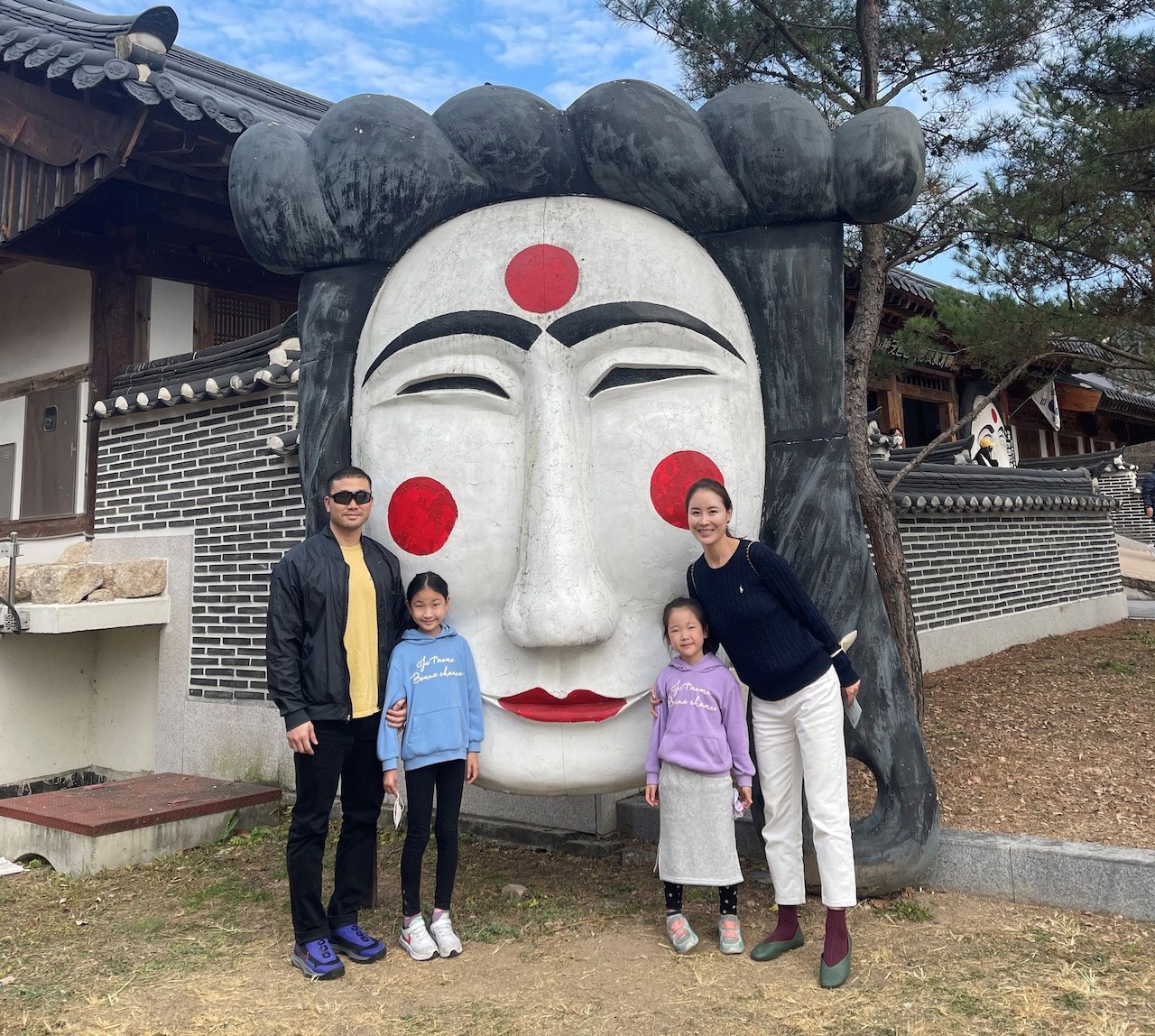 A couple and their two daughters stand in front of a large mask.