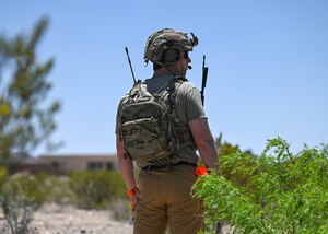 A man wearing a radio and camouflaged equipment stands in an open area.
