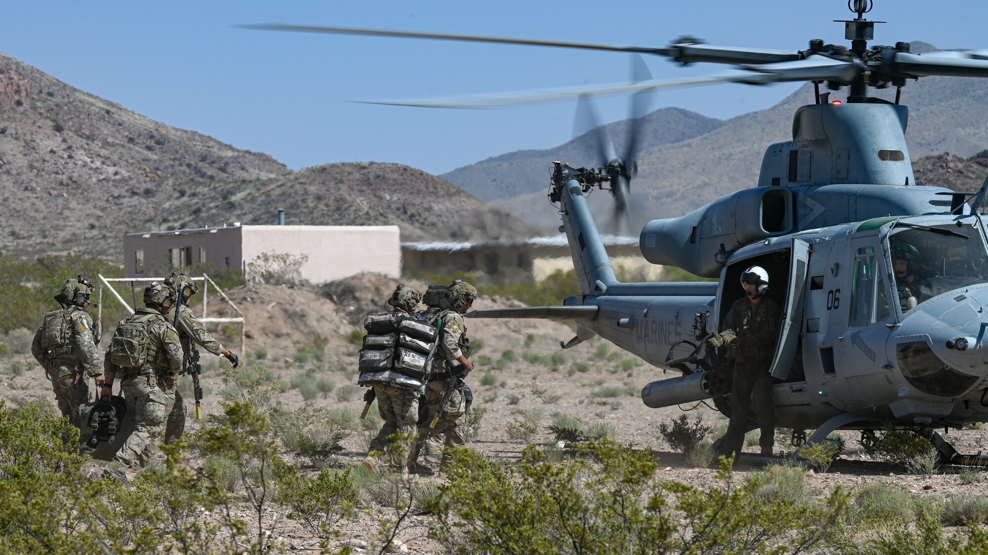 Men in military uniforms carrying equipment board a helicopter,