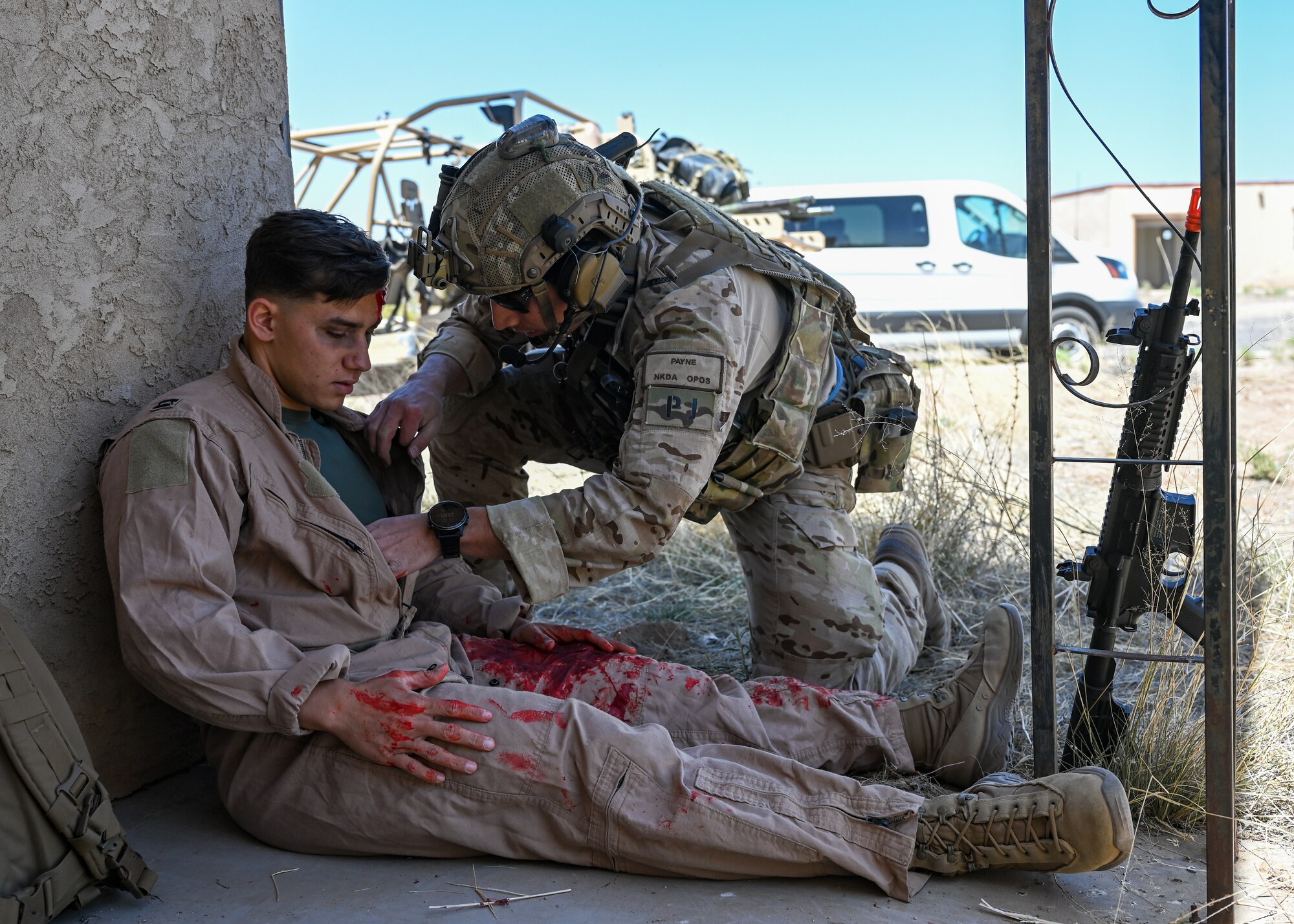 A man in a military uniform checks a simulated car crash victim for injuries.