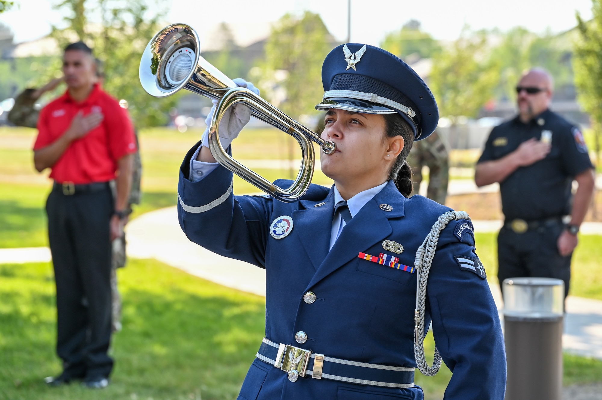 An Airman blows a bugle while others place their hand over the heart