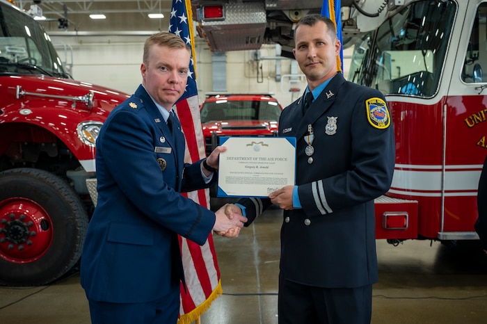 Maj. Nathan Thomsen shakes hands with Capt. Greg Arnold while awarding him a certificate.