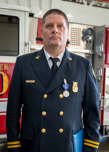 District Chief David Warner stands at attention in front of a fire truck.