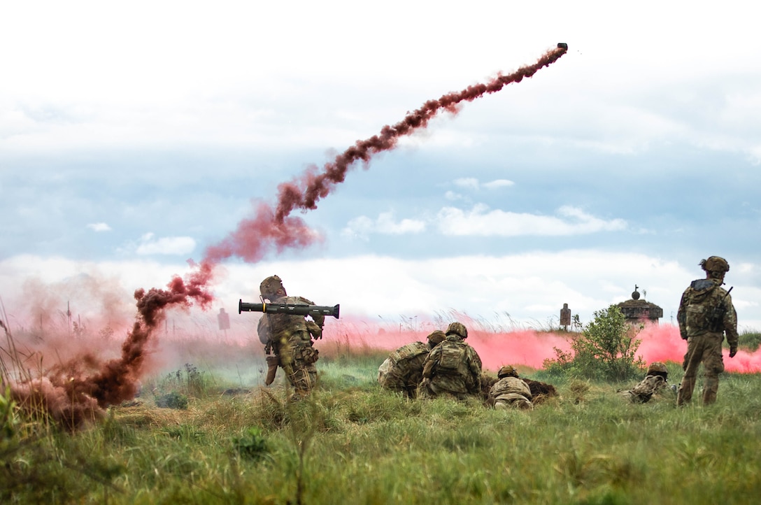 A grenade flies through the sky above soldiers in a field, leaving a curved arc of reddish smoke.