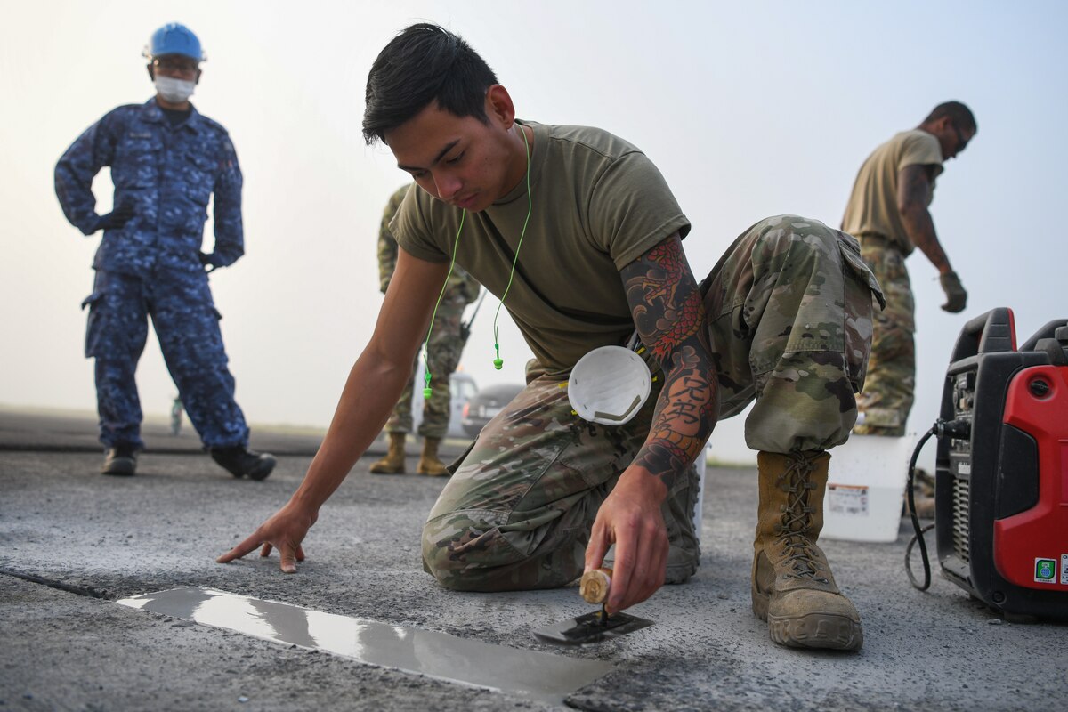 Airman 1st Class John Olarte, 374th Civil Engineering Squadron pavement and heavy equipment journeyman, flattens out wet concrete as part of a spall repair at Kanoya Air Base, Japan, May 15, 2023. A four-man team from Yokota Air Base traveled to Kanoya to teach Japan Maritime Self-Defense Force engineers how to complete a spall repair. (U.S. Air Force photo by Staff Sgt. Spencer Tobler)