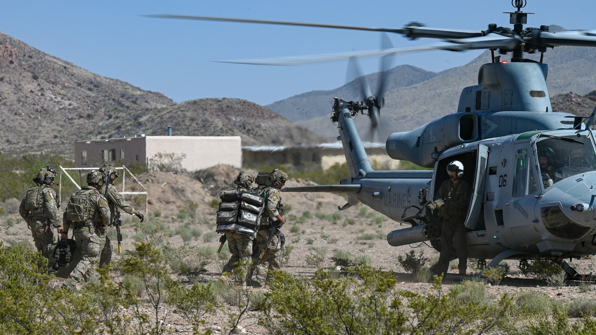 Men in military uniforms carrying equipment board a helicopter,