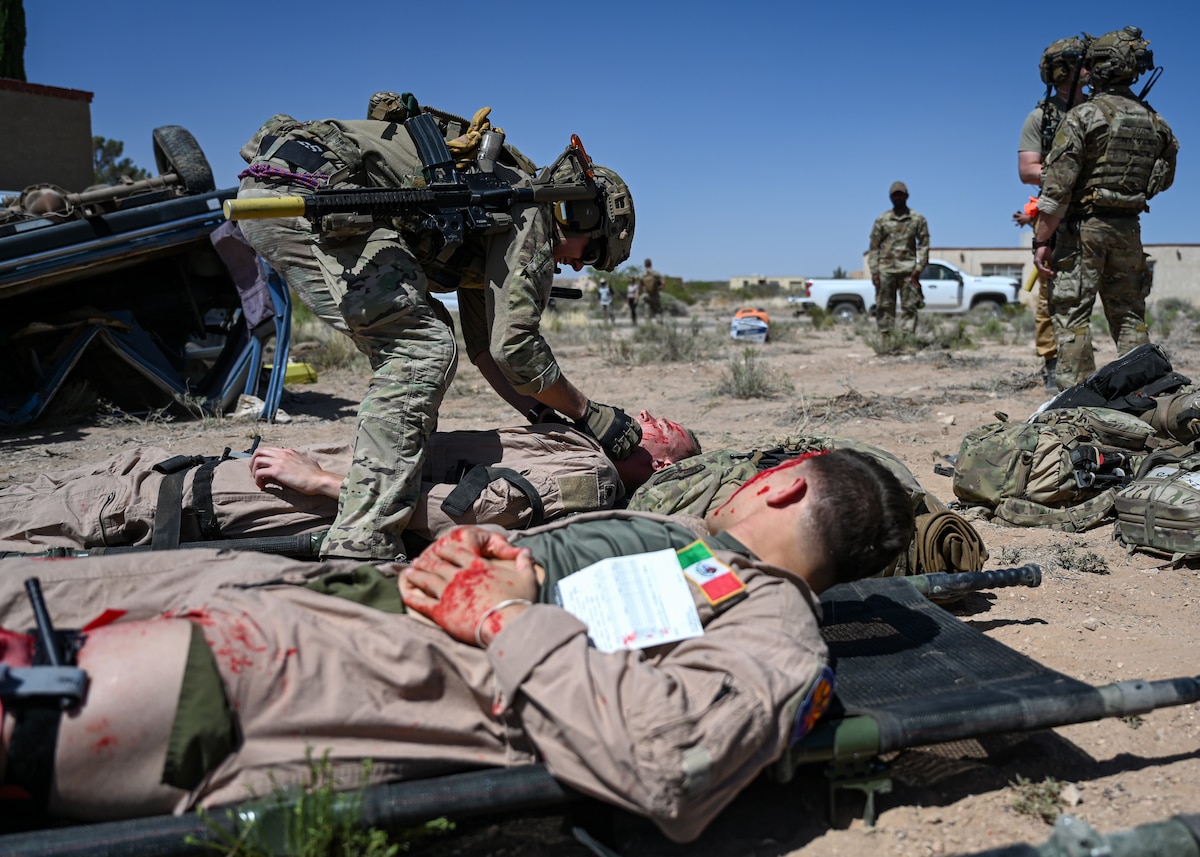 A man in a military uniform provides care to a simulated car crash victim.